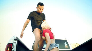 A blonde is on the back of a truck and she is getting licked well