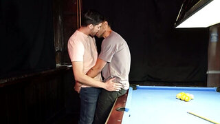 Two men with big cocks are banging a lad on the table