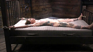 Inked lady is spread out on the bed, tied up and tortured